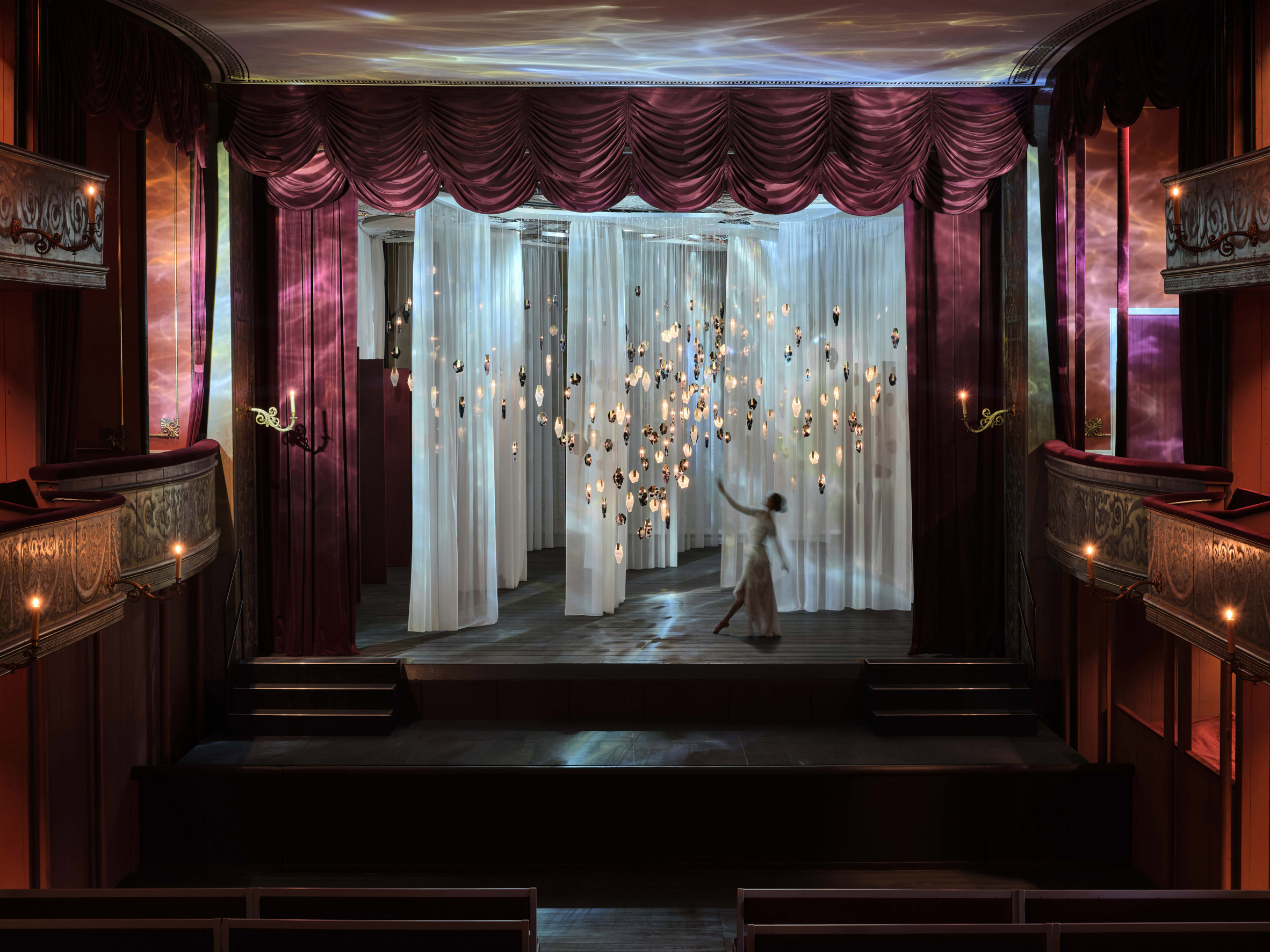 Crystal-like pendant lights suspended in front of translucent white curtains inside theatre