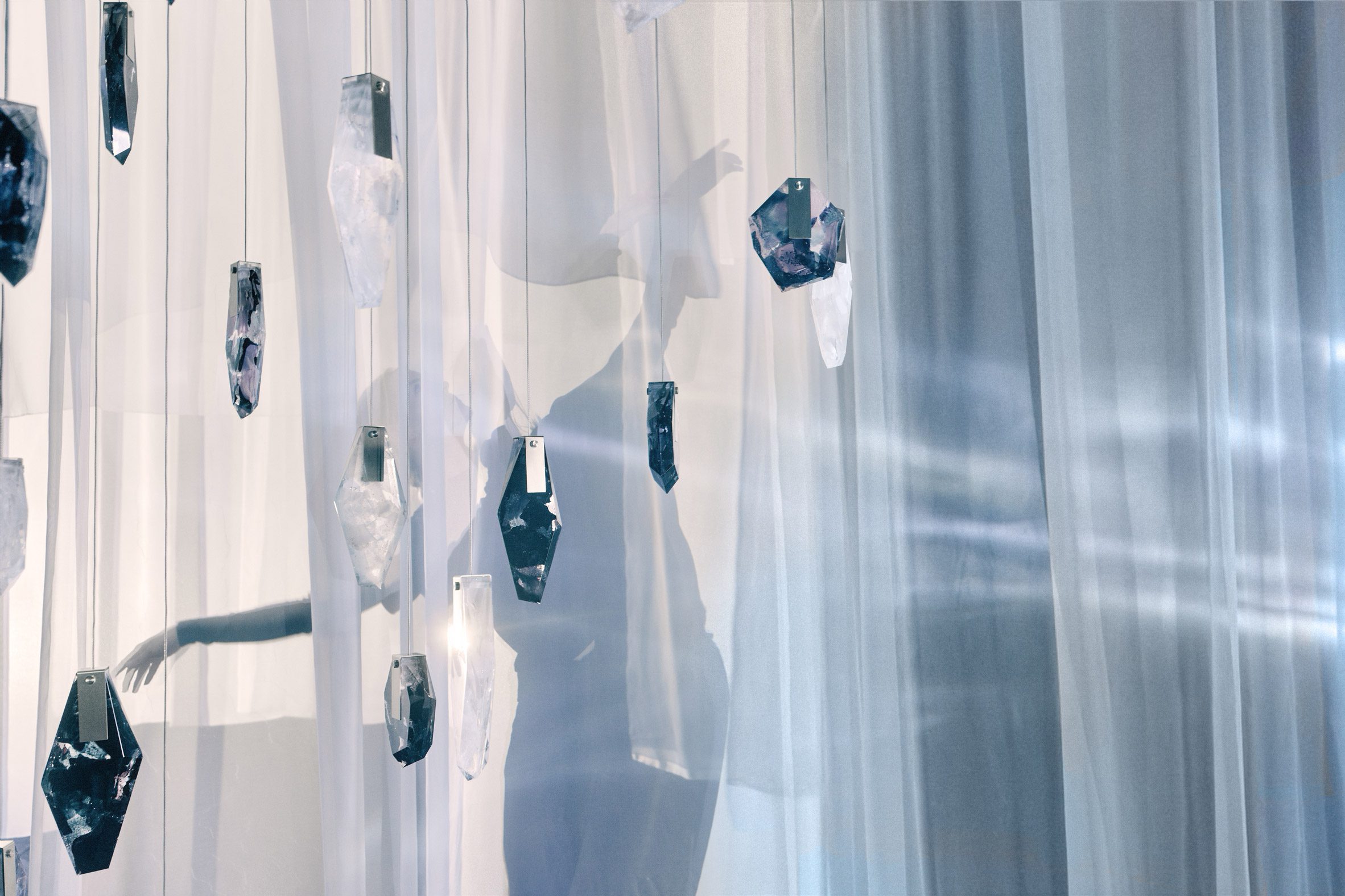 Suspended illuminated glass forms casting reflections across translucent curtains