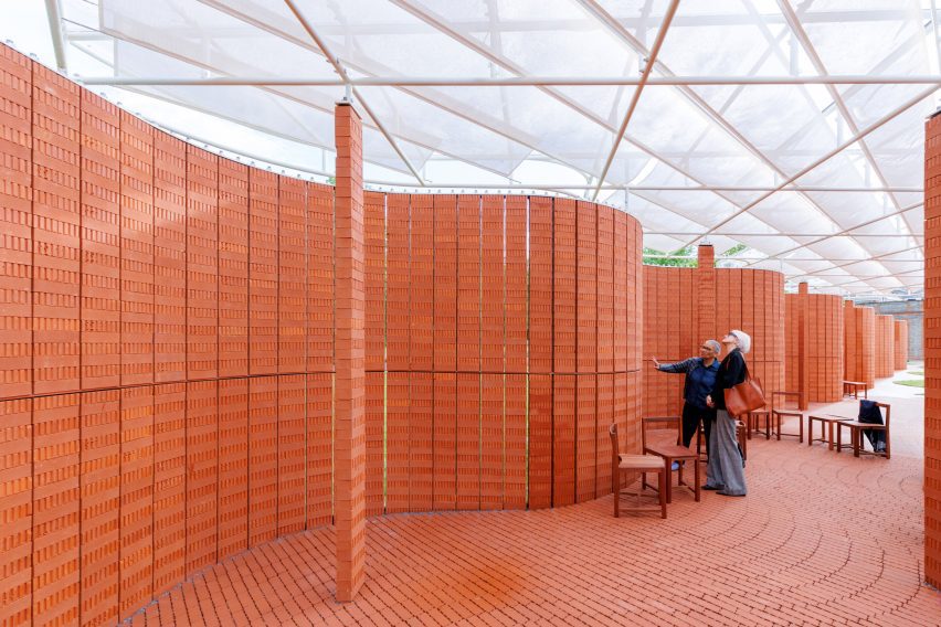 Visitors standing inside the pavilion among curving brick walls beneath a lightweight white canopy