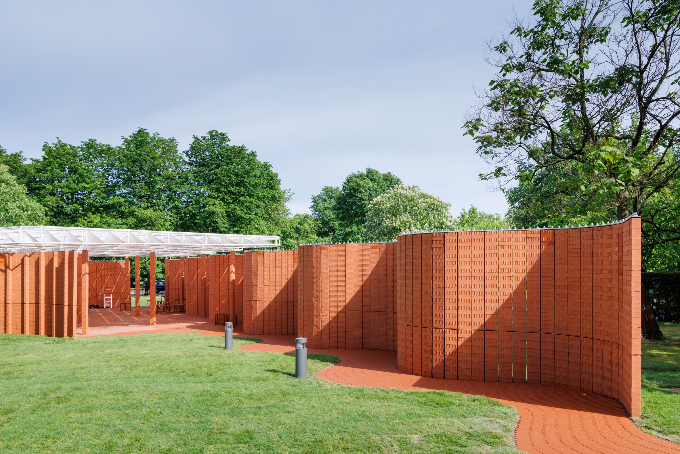 Curving red-brick walls creating a winding route around a central open space beneath a white canopy