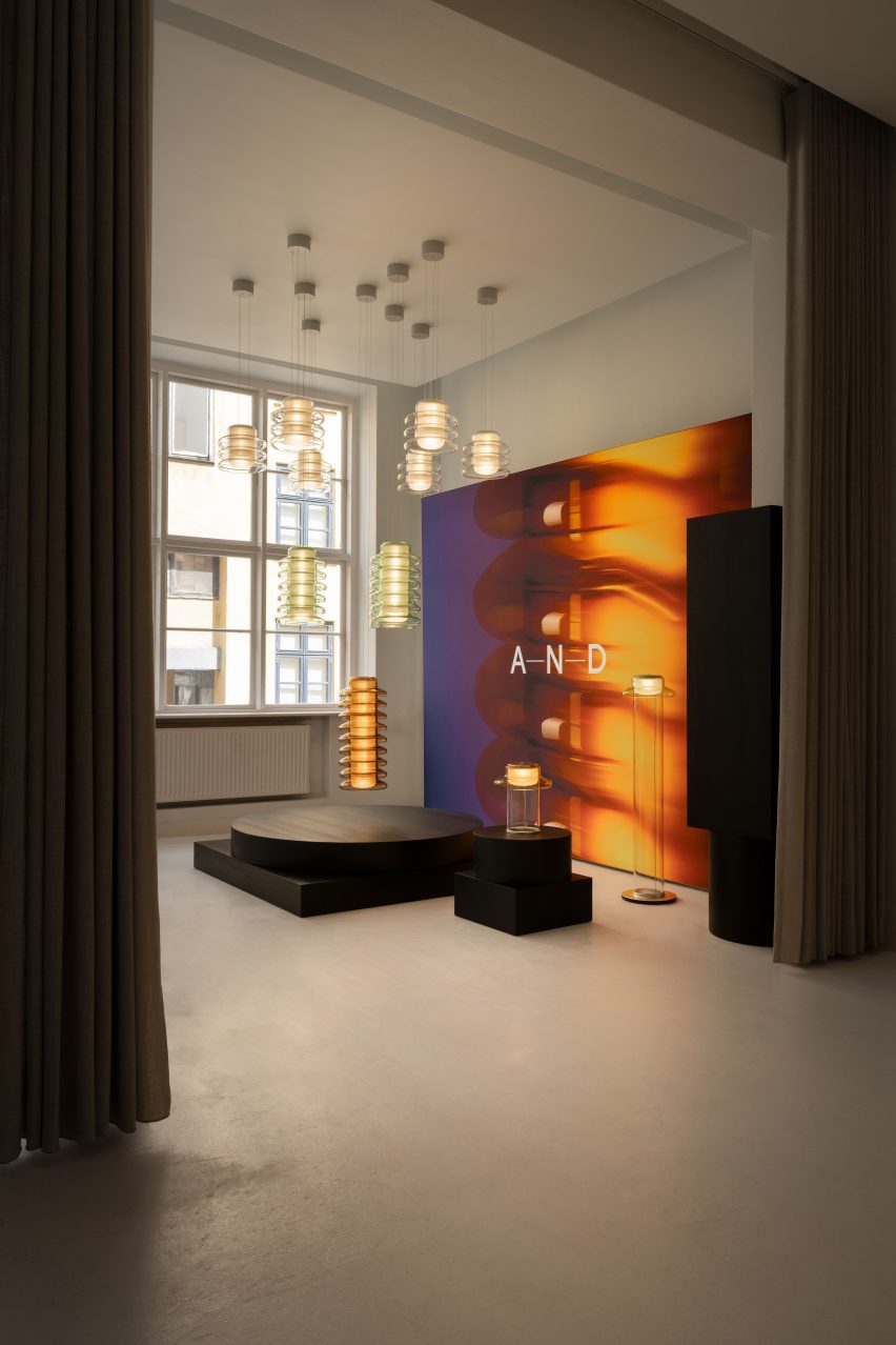 View into a gallery space displaying suspended cylindrical pendant lights