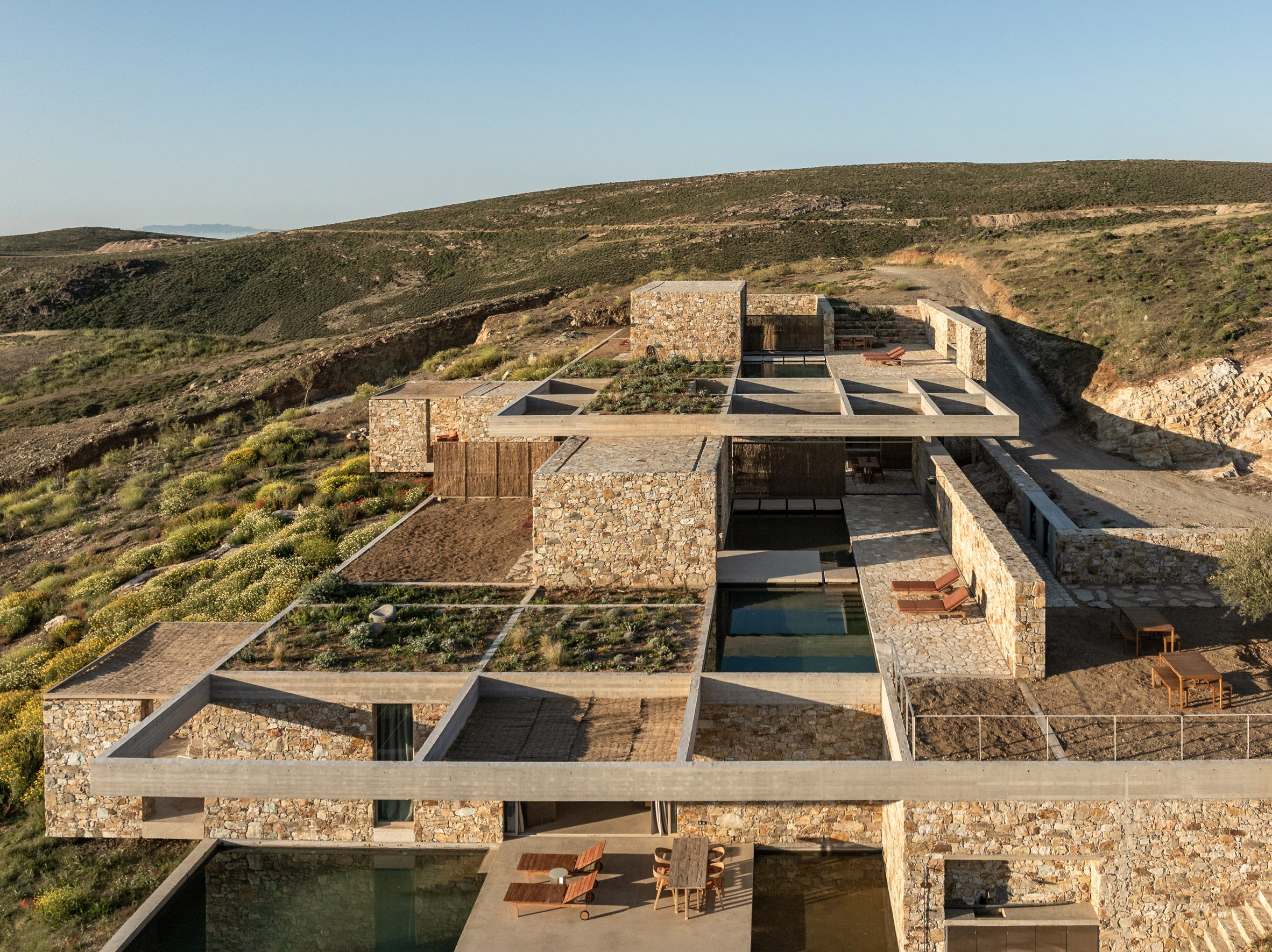 Los edificios revestidos de piedra y los techos ajardinados están dispuestos bajo una estructura de rejilla de hormigón.
