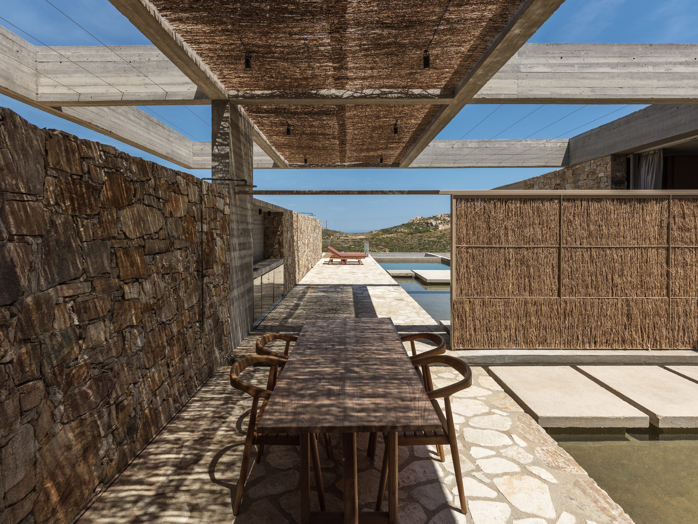 El comedor al aire libre está sombreado por una pantalla de caña y enmarcado por un muro de piedra.