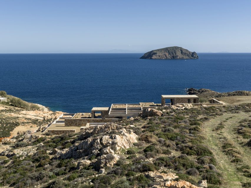 Stone accommodation units embedded into a coastal hillside overlooking the Aegean