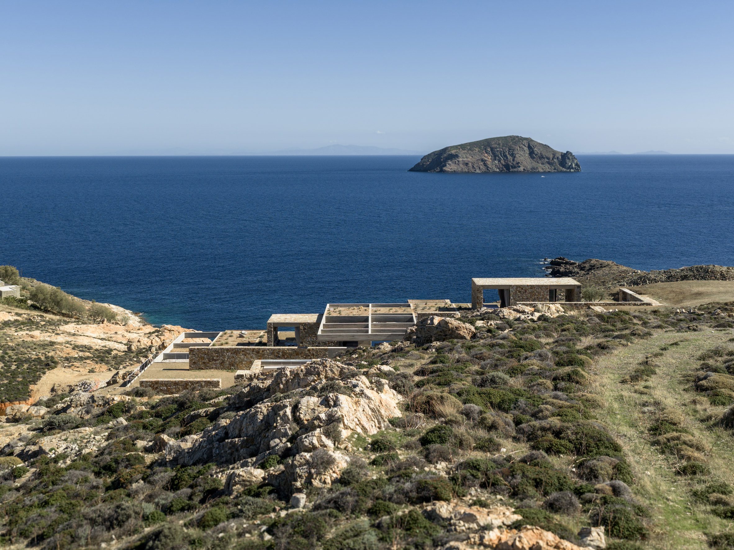 Las unidades de alojamiento de piedra están incrustadas en la ladera costera con vistas al mar Egeo.