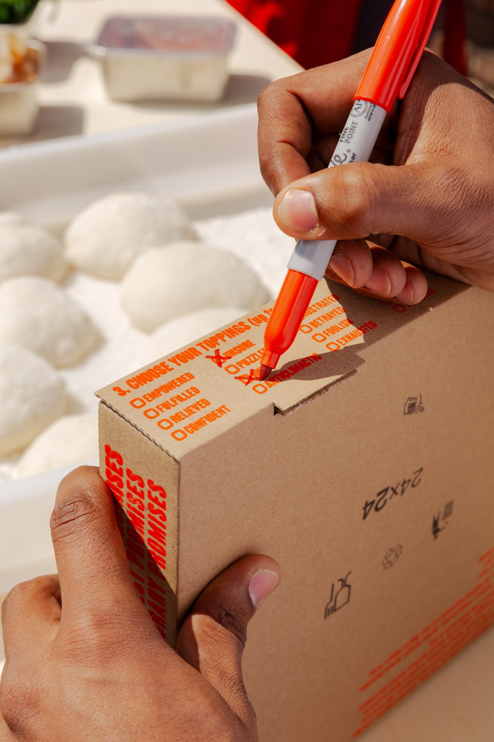 Foto de primer plano de las manos de una persona llenando una lista de casillas de verificación al costado de una caja de pizza con las palabras 