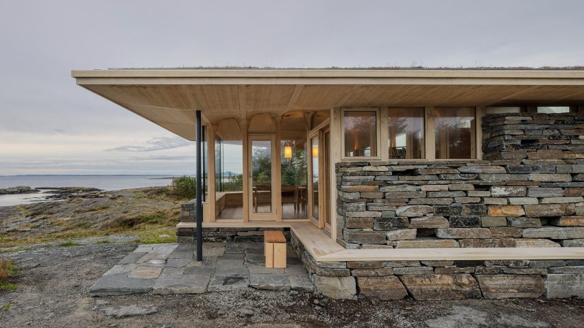 Corner of the timber cabin showing projecting roof, stone plinth and large glazed openings