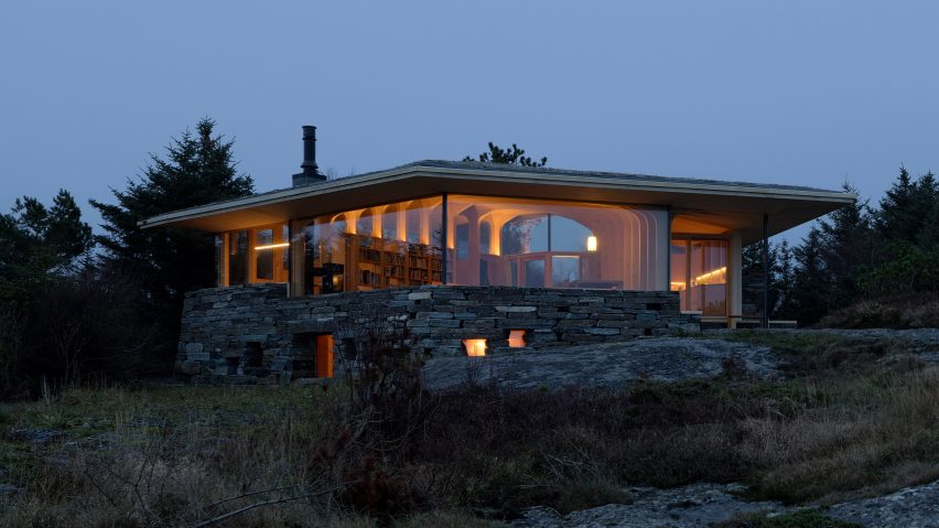 Evening view of the illuminated timber cabin resting on a stone base within the coastal landscape