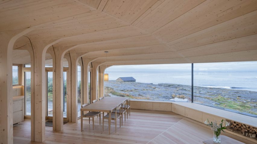 Timber dining space overlooking the rocky coastline through a wide panoramic window