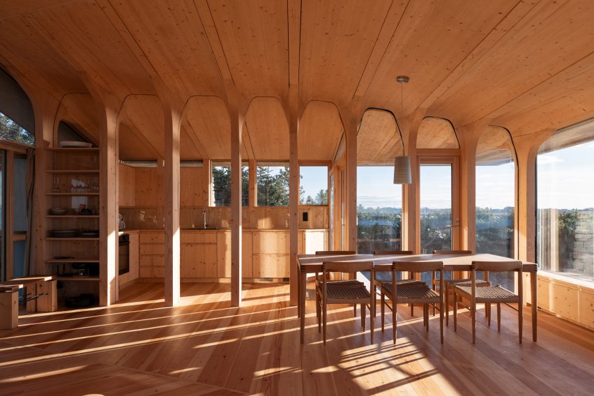 Open-plan timber interior with tree-like columns supporting the ceiling around the dining area and kitchen