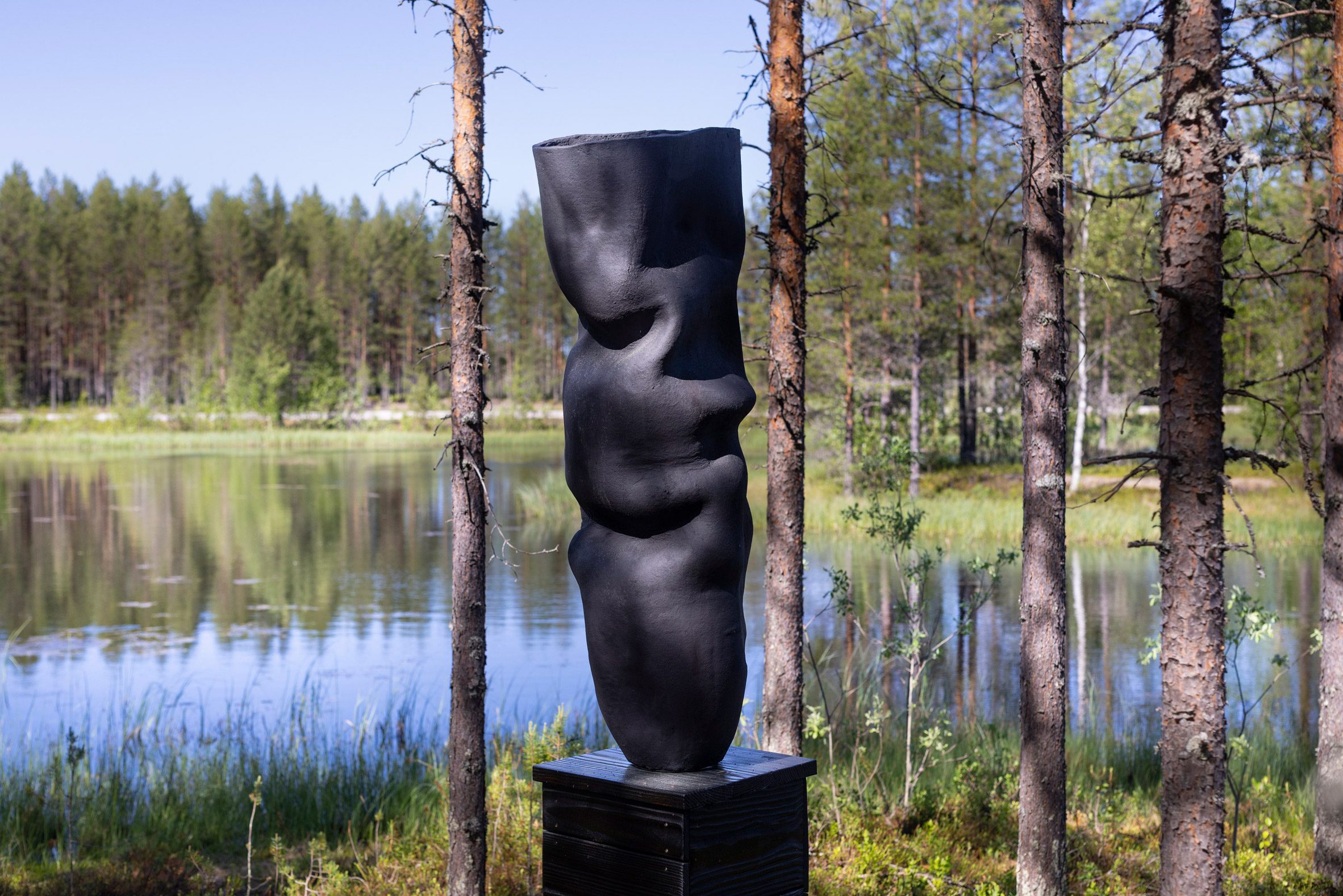 La foto de la obra de arte Climate Clock de Ranti Bam muestra una enorme vasija de cerámica negra tallada con suaves pliegues en la orilla de un lago.