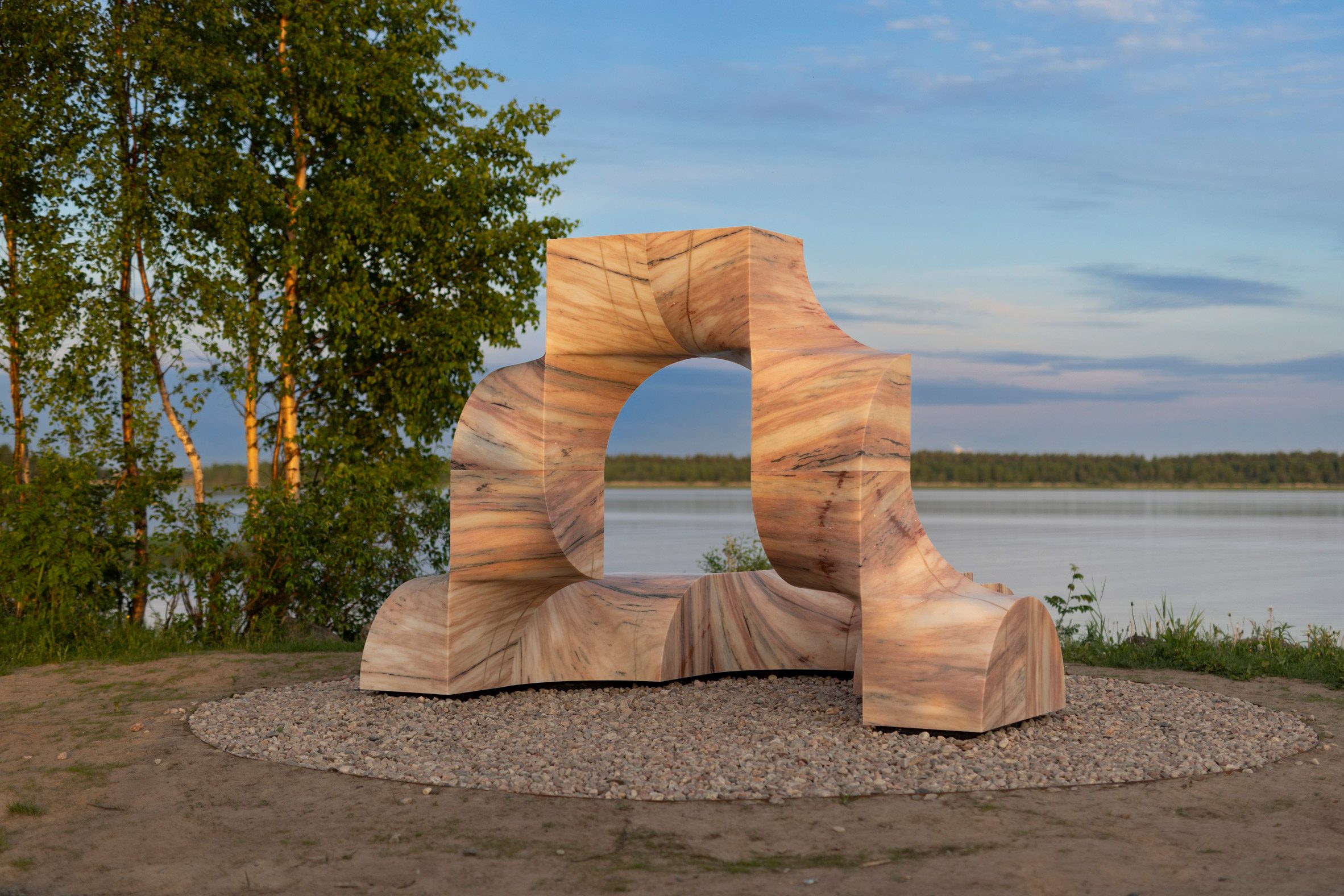 Foto de la escultura de mármol rosa Super Kelo ubicada junto al puerto rodeada de árboles y césped.
