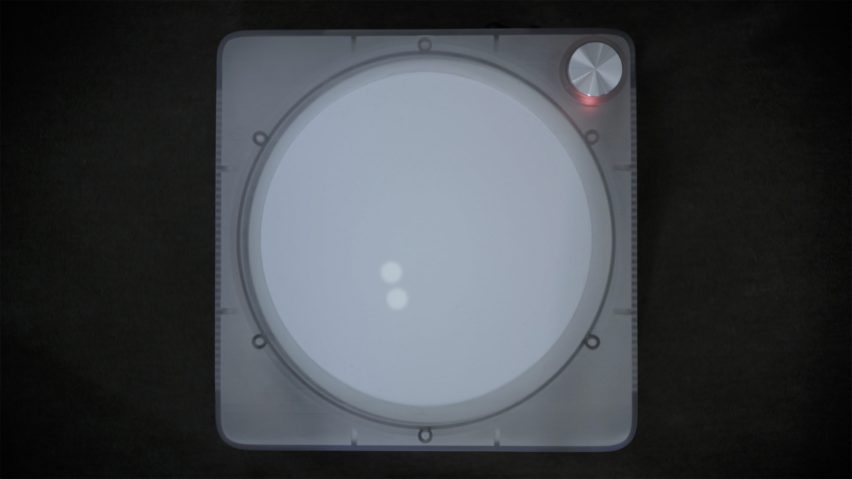 Overhead view photo of the Imago device, showing a record player-like gadget with a simple white circular touchscreen lit up with two glowing dots