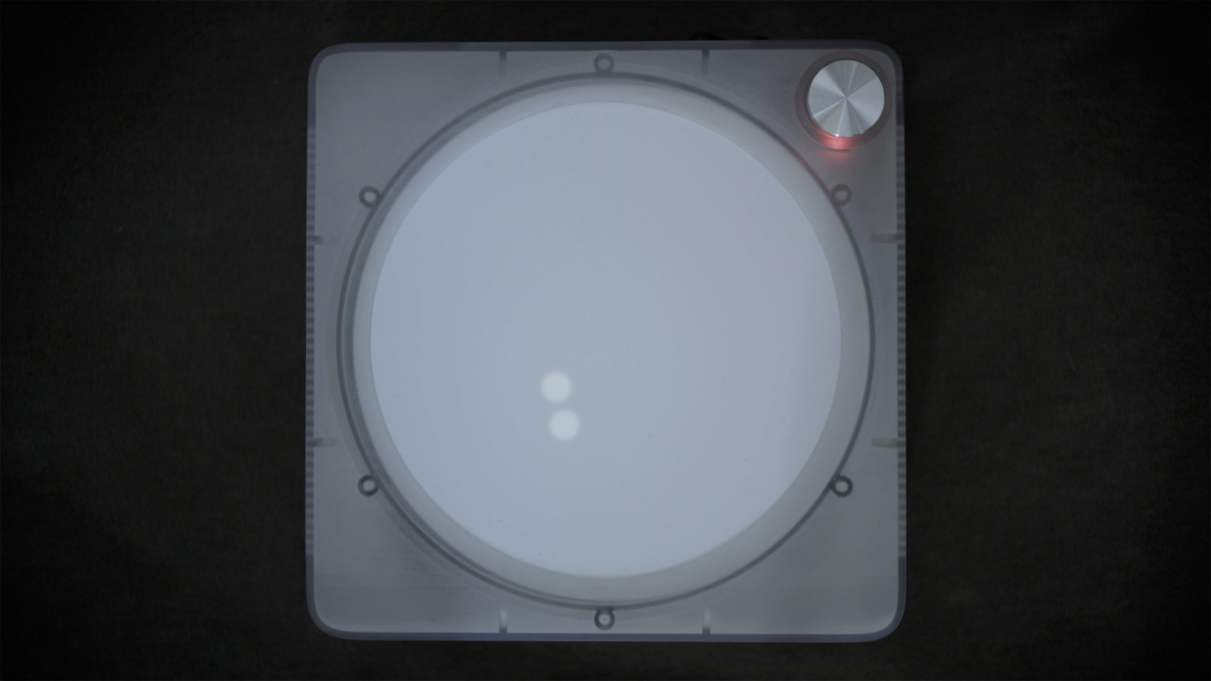Overhead view photo of the Imago device, showing a record player-like gadget with a simple white circular touchscreen lit up with two glowing dots