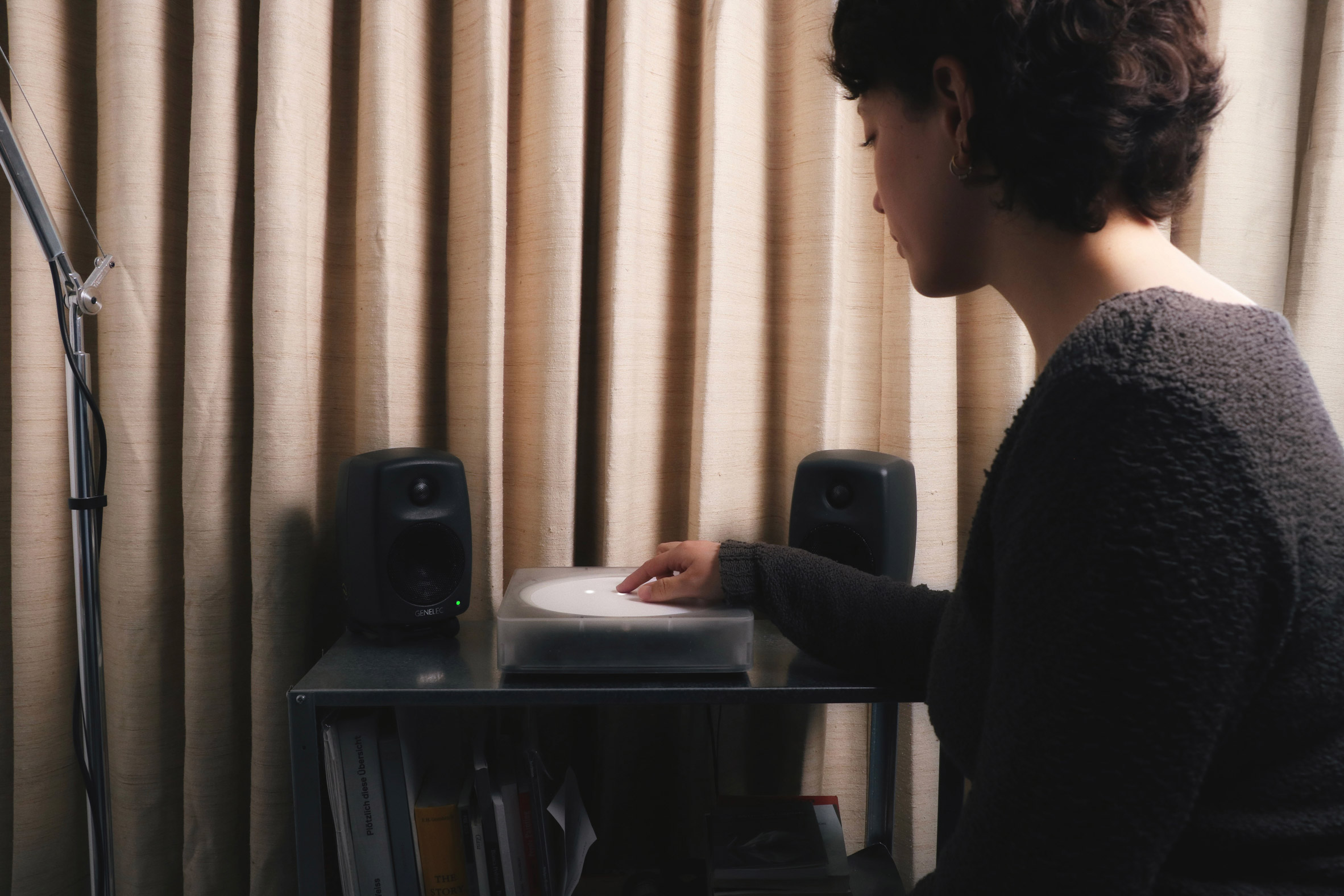 Photo of a woman in a cosy home environment using the Imago device positioned on a small shelf with speakers