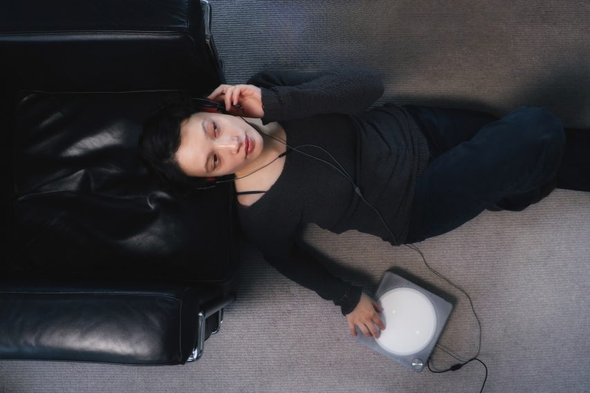 Photo of a woman sitting in repose while wearing headphones, with her fingers resting on a the circular white touchscreen of the Imago audio player