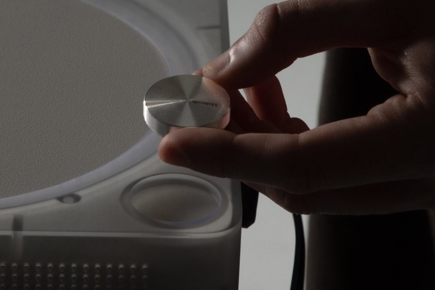 Close-up photo of a small metal puck being placed into a circular slot on the corner of the Imago audio player