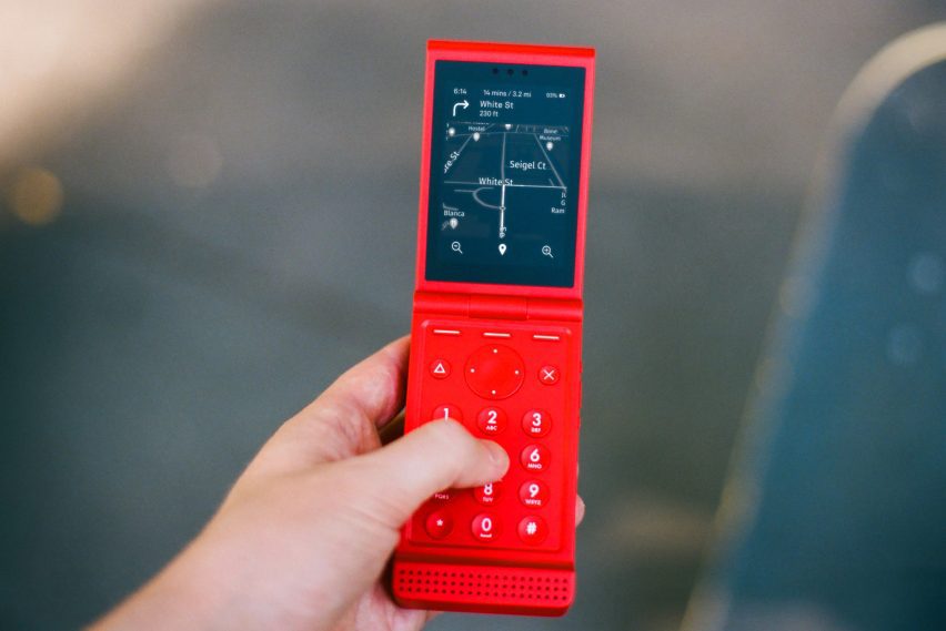 Photo of a red Light Flip phone in someone's hand showing a map with direction on a monochrome, mostly black screen
