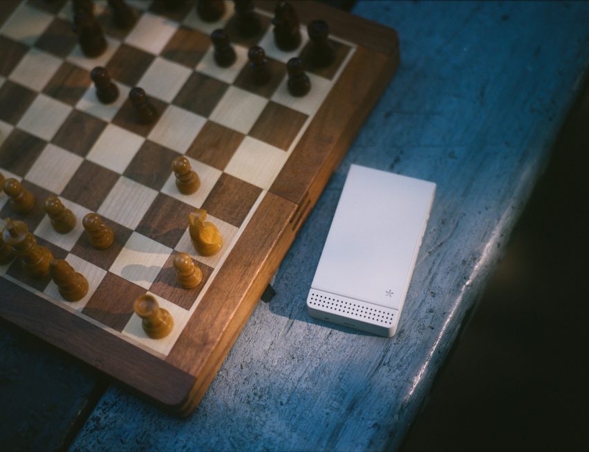 Photo of a white Light Flip phone closed and sitting on a table next to a chess board mid-play