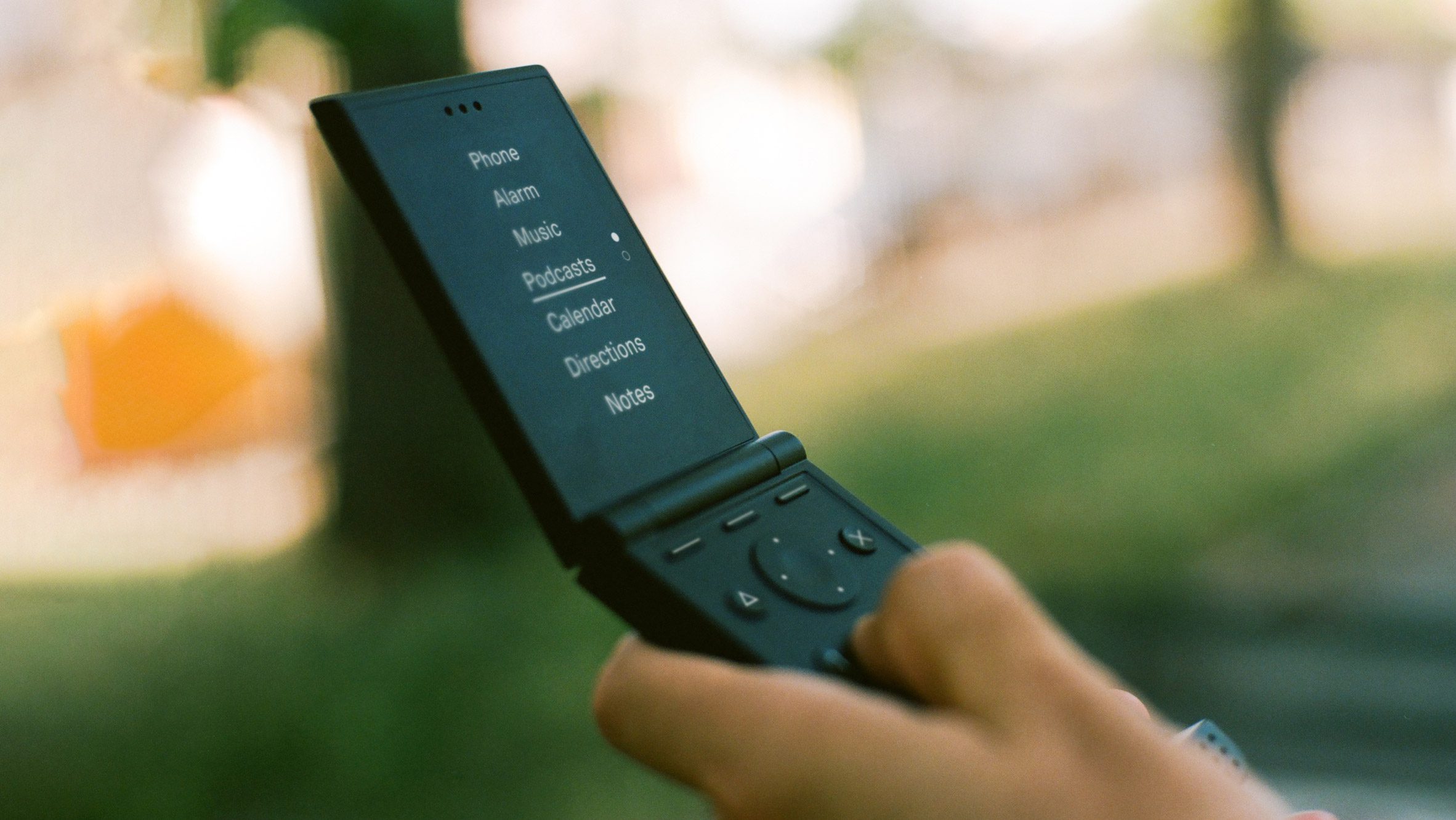 Photo of a black Light Flip phone in someone's hand as they scan a list of apps written in white text on a black background on the screen
