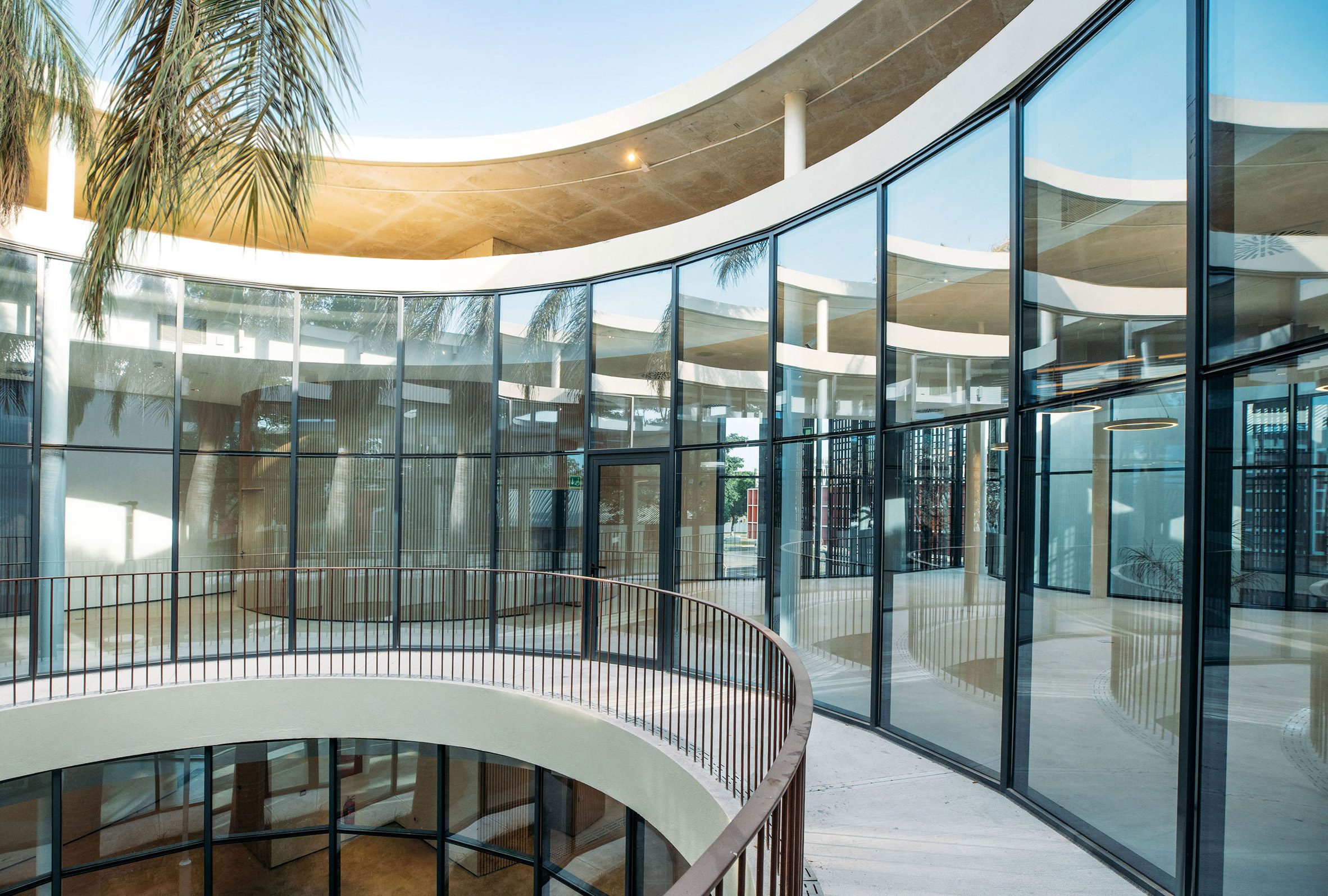 Curved glazed walkway overlooking a circular courtyard beneath the overhanging concrete roof