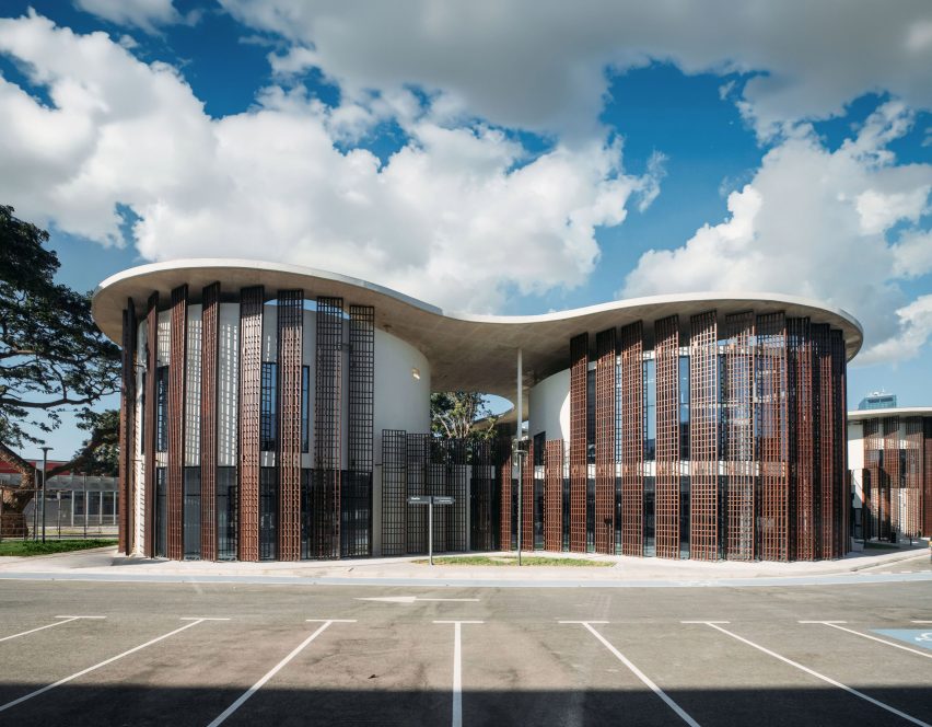 Exterior view of curved white volumes screened by vertical aluminium fins beneath a concrete canopy