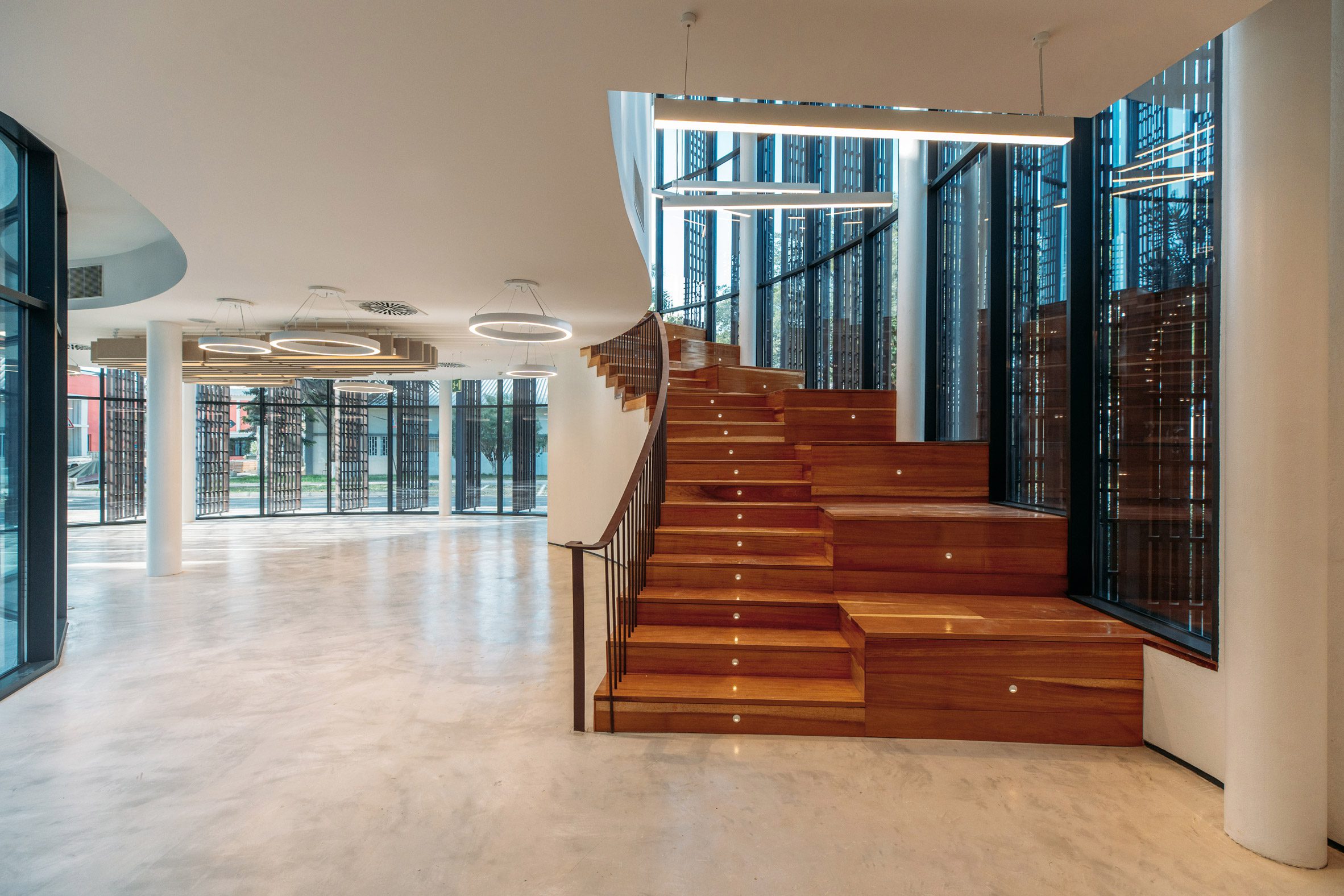 Open interior featuring a wide timber staircase leading to the upper floor beside curved glazed walls