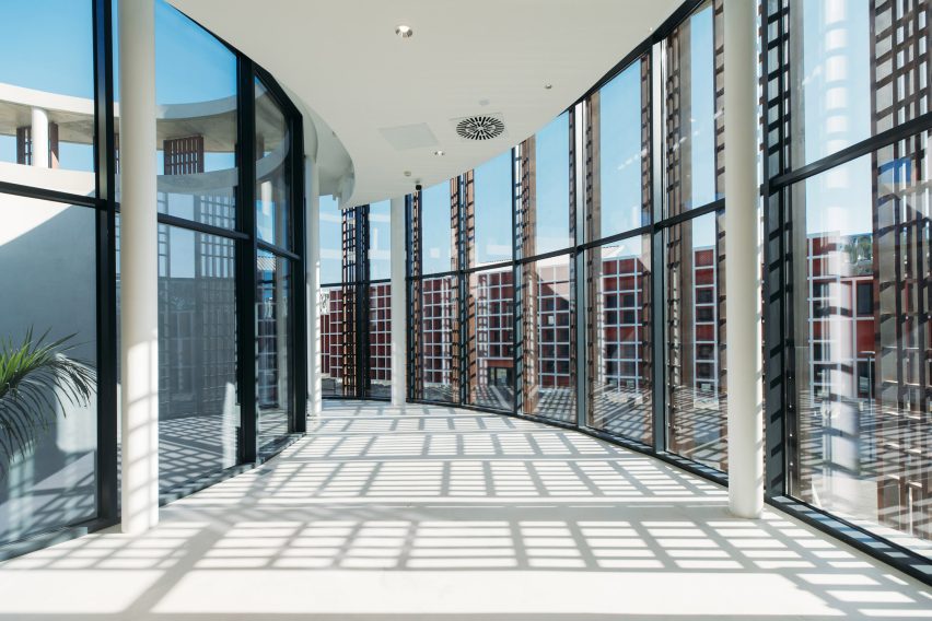 Curved interior corridor with full-height glazing and patterned shadows cast across the floor