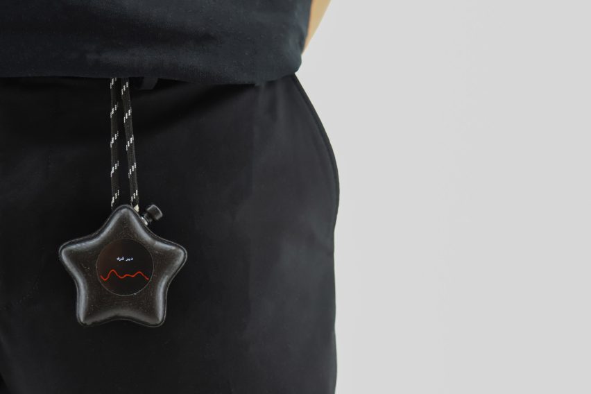 Photo of a black star-shaped Mesh-89 device attached by a tether to a person's waistband