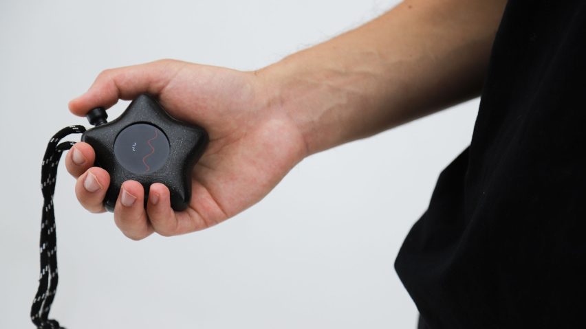 Photo of a person's arm holding a black star-shaped Mesh-89 device with a red wavy line across the screen
