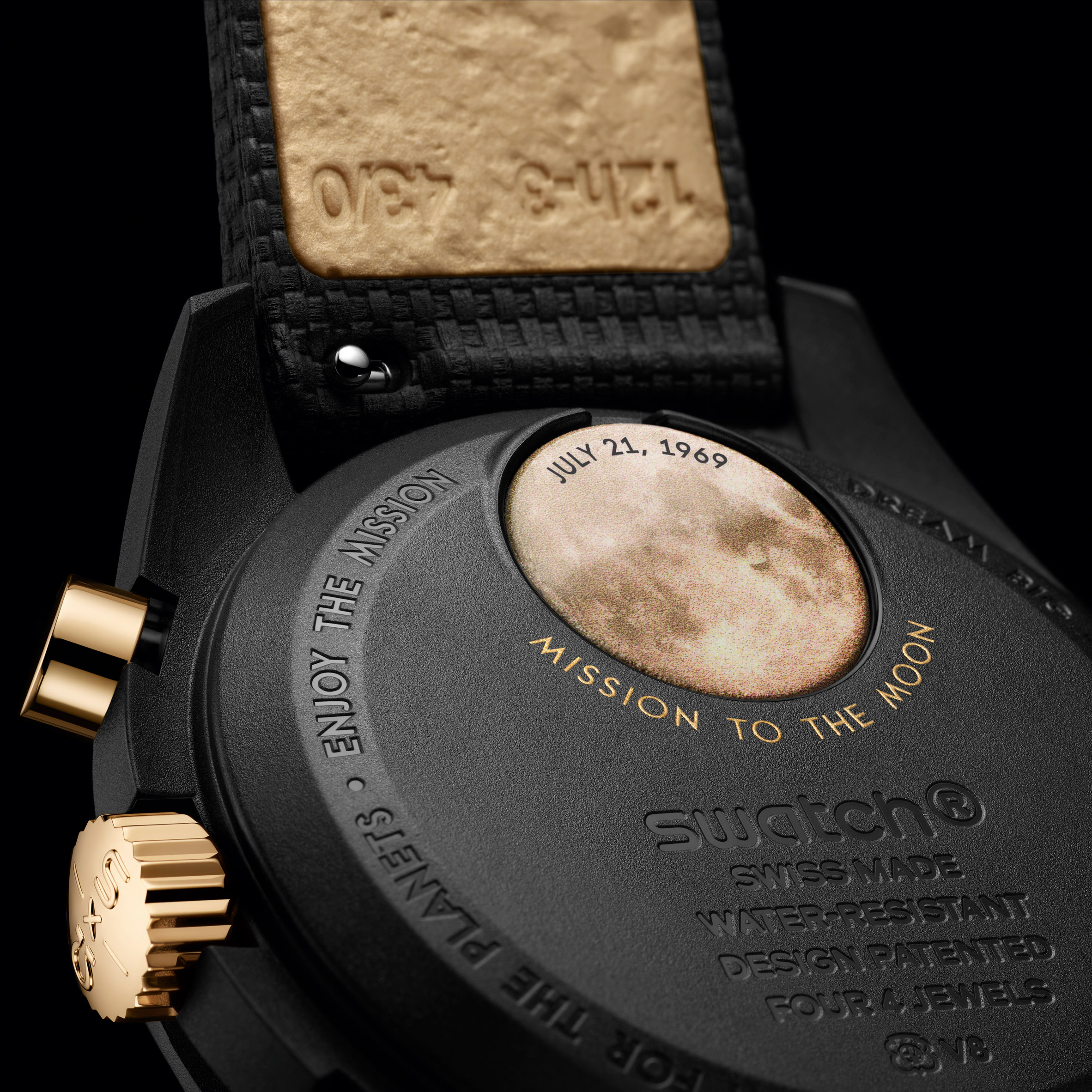 Close-up image of the reverse of the Swatch x Omega MoonSwatch showing reverse of the gold MoonSwatch showing a gold moon battery cover on the black case inscribed with Mission to the Moon in gold letters and the date July 21, 1969 on the moon
