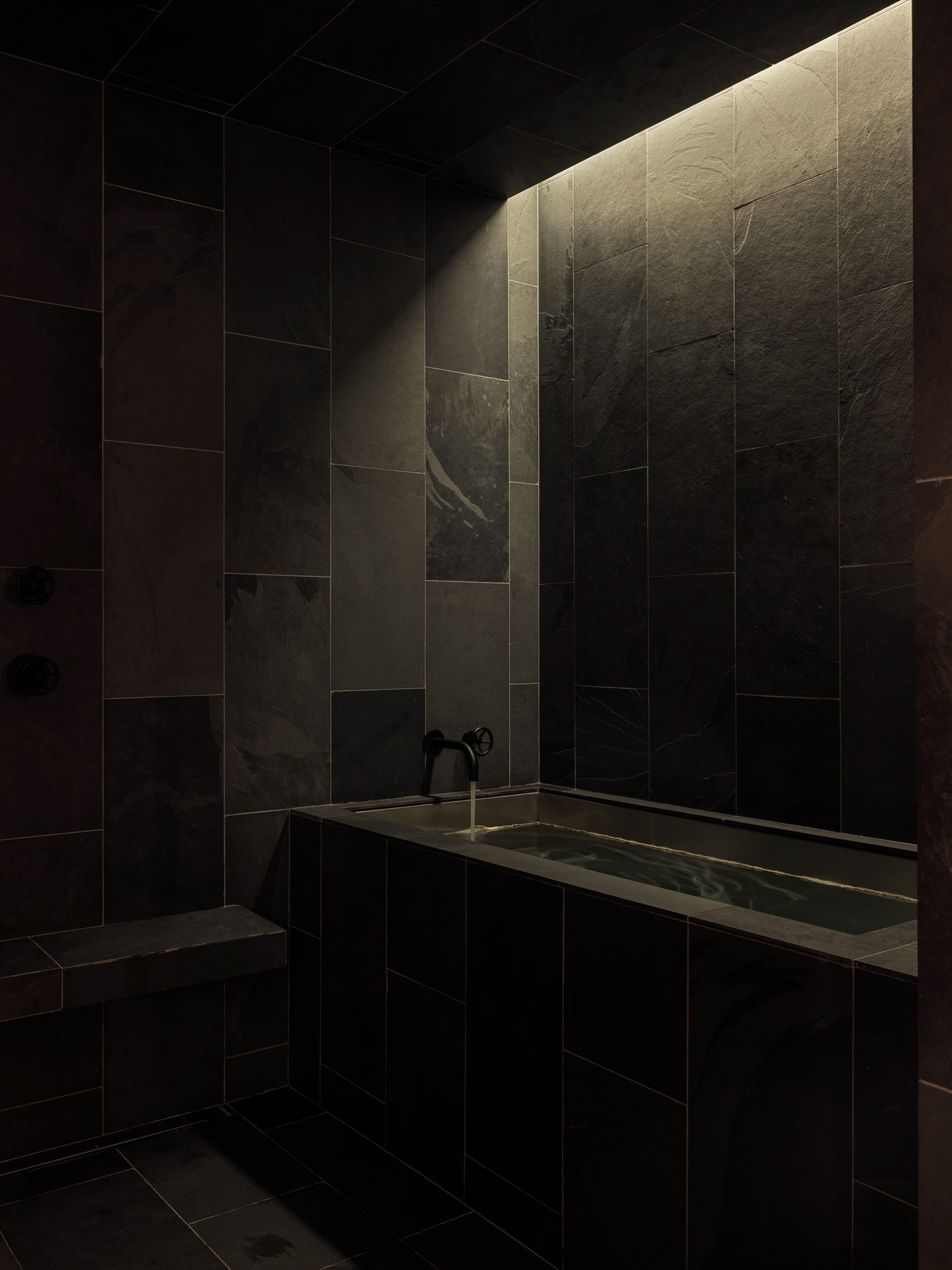 A single shaft of light above a bath highlights the texture of slate