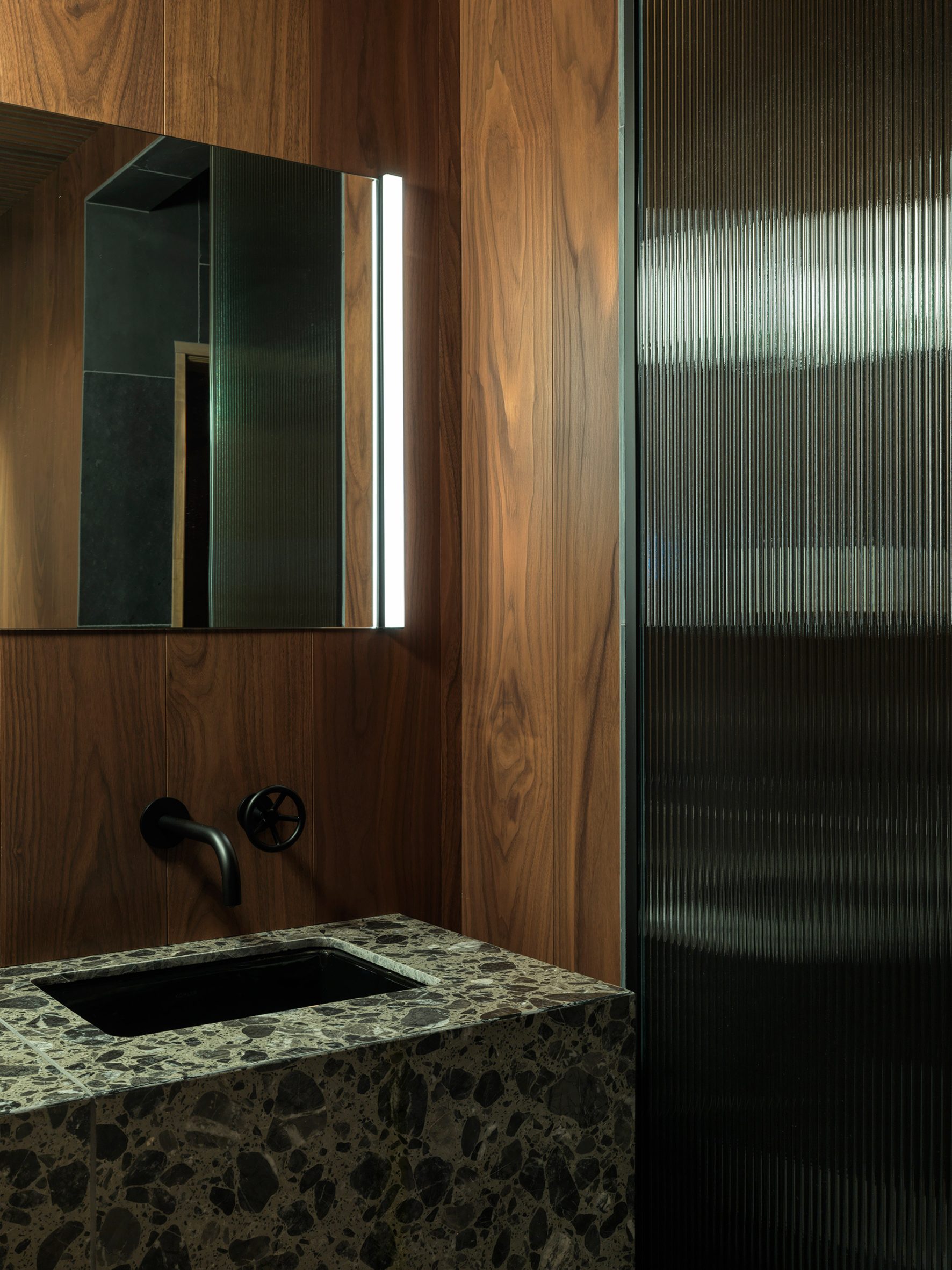 A terrazzo vanity and fritted glass partition within a changing room