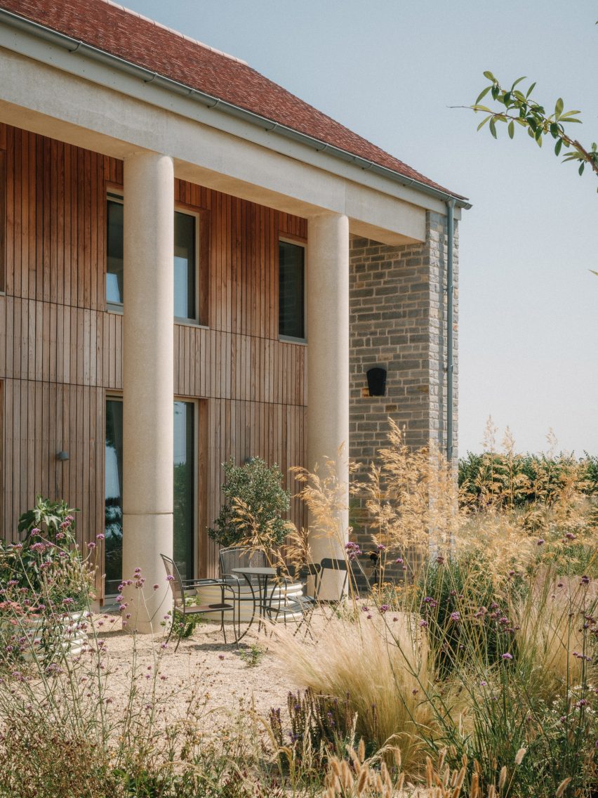 Corner view of the house showing cylindrical concrete columns, timber cladding, stone walls and planting around the sheltered terrace