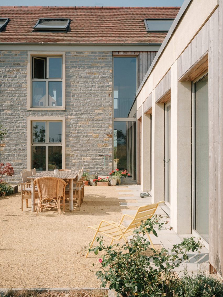 Courtyard beside the house with stone walls, timber cladding, sliding glazed doors and outdoor dining furniture