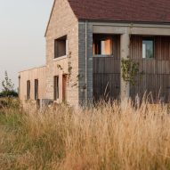 Side view of the farmhouse-style home with pale stone walls, timber cladding and a pitched roof surrounded by long grasses