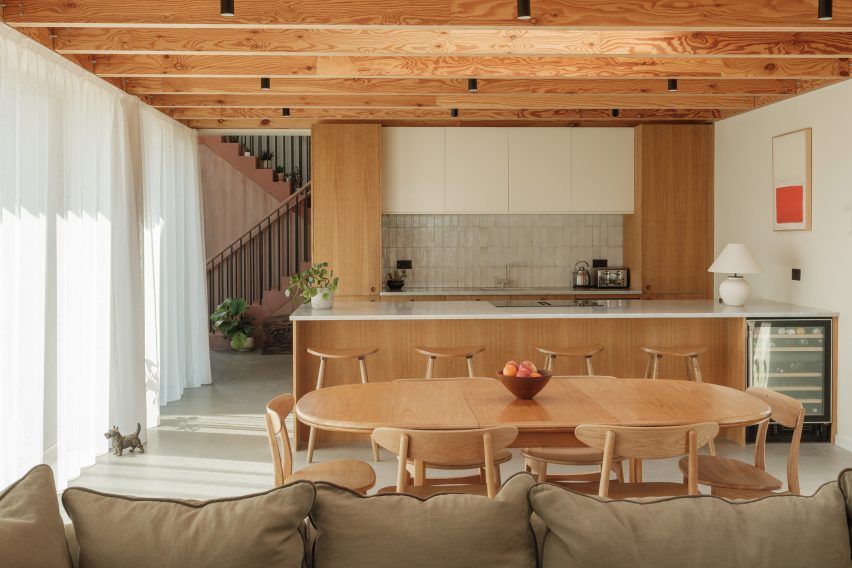 Open-plan kitchen and dining space with exposed timber beams, cherry cabinetry, polished concrete floor and a large dining table