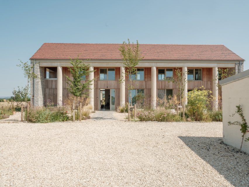Front elevation of the two-storey house with a pitched roof, concrete colonnade, timber facade and planting in the foreground
