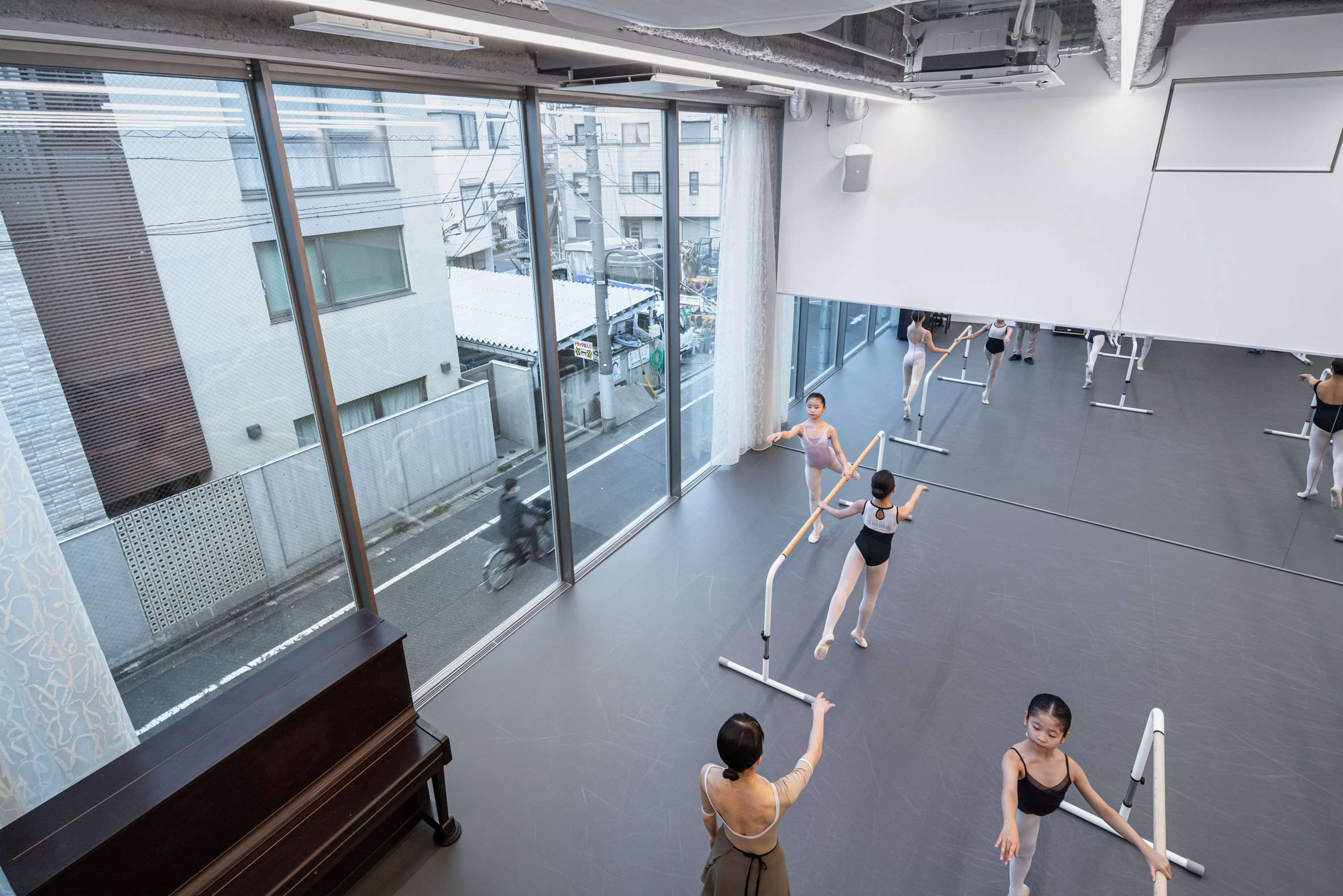 Interior del estudio de ballet con bailarines practicando, con vistas a la calle.
