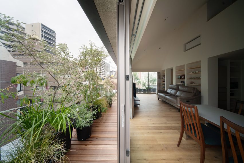 Sliding doors open from the living room onto a planted timber terrace surrounding the upper floor