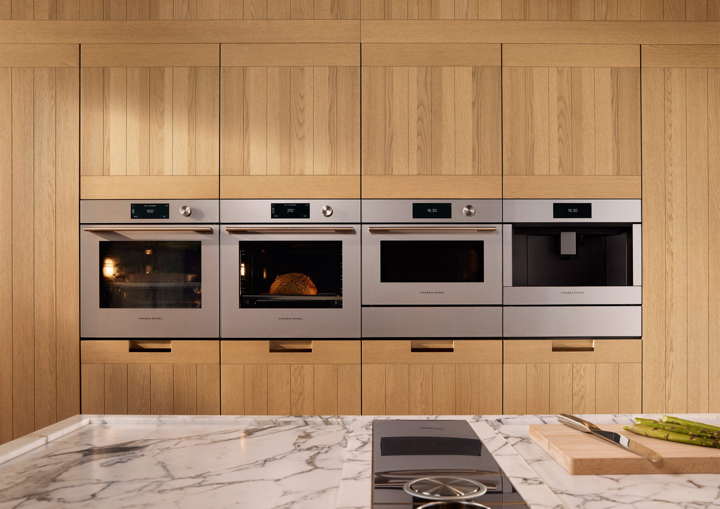 Image of a large kitchen with golden wood cabinetry and four Fisher & Paykel ovens installed in a row
