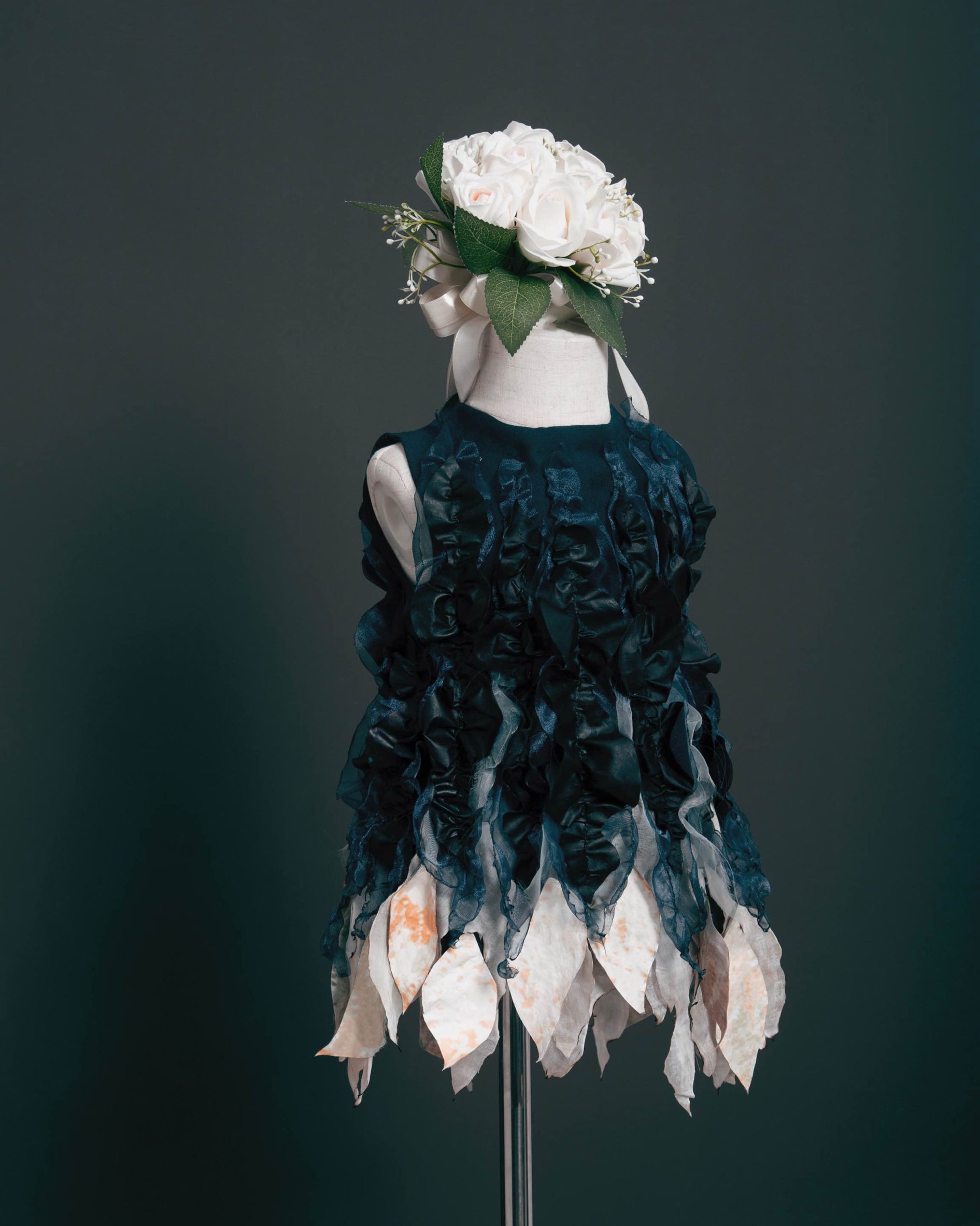 Photo of a dark blue dress with white ruffles on the bottom hem, sitting on a mannequin