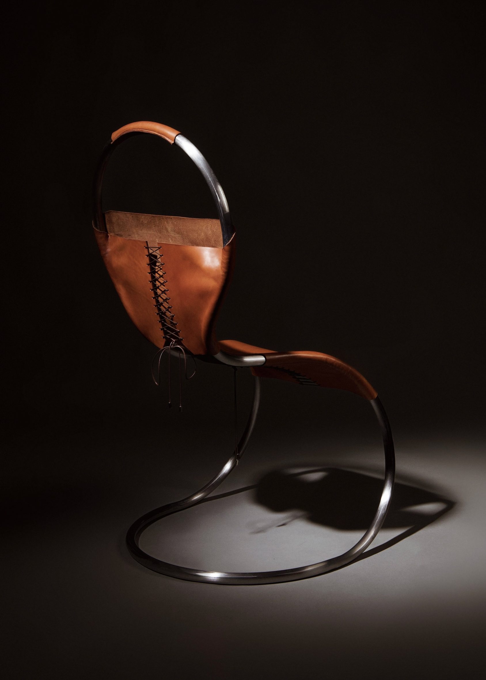 Picture showing a steel framed chair with a brown leather corset tied around it, secured with brown cord in a criss cross pattern.