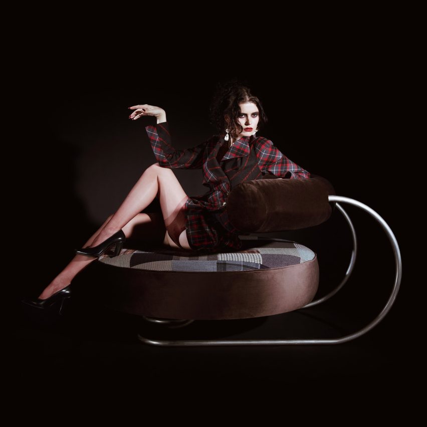 A person is laid across a large circular seat with a brown, curved, cylindrical back stop that is held up by a steel frame. The circular seat has patchwork upholstery.