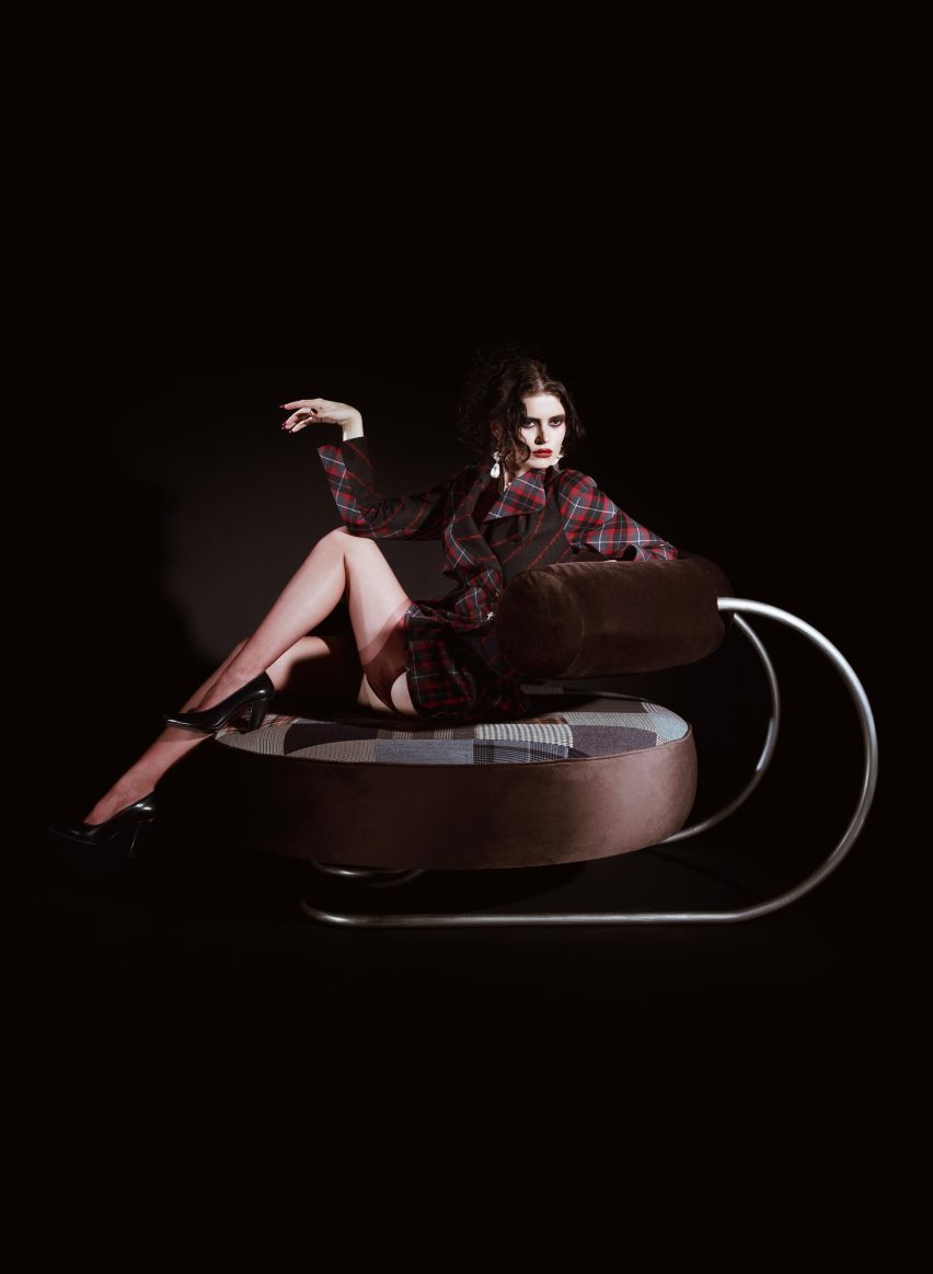 A person is laid across a large circular seat with a brown, curved, cylindrical back stop that is held up by a steel frame. The circular seat has patchwork upholstery.