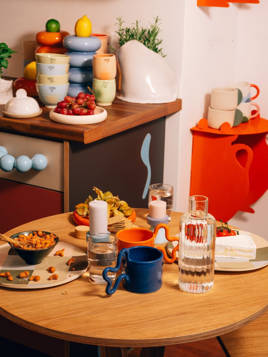 Close-up photo of the small circular wooden dining table at the UAL Atterbury Flat laden with ceramic dishes and food, with a colourful kitchen viewable in the background 
