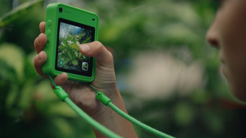 Close-up photo of the screen of a Freckle phone in a forest setting while a child snaps a photo of some foliage
