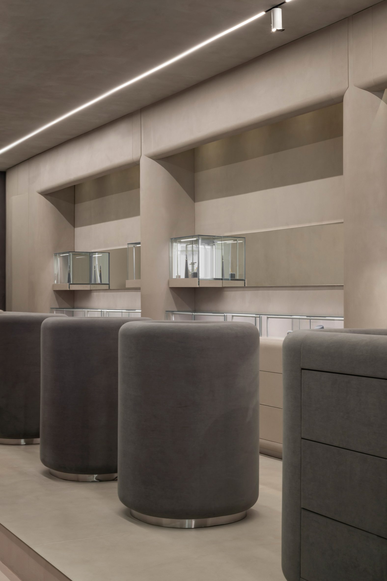 A series of centrally positioned vitrines feature rounded edges and are upholstered in grey suede
