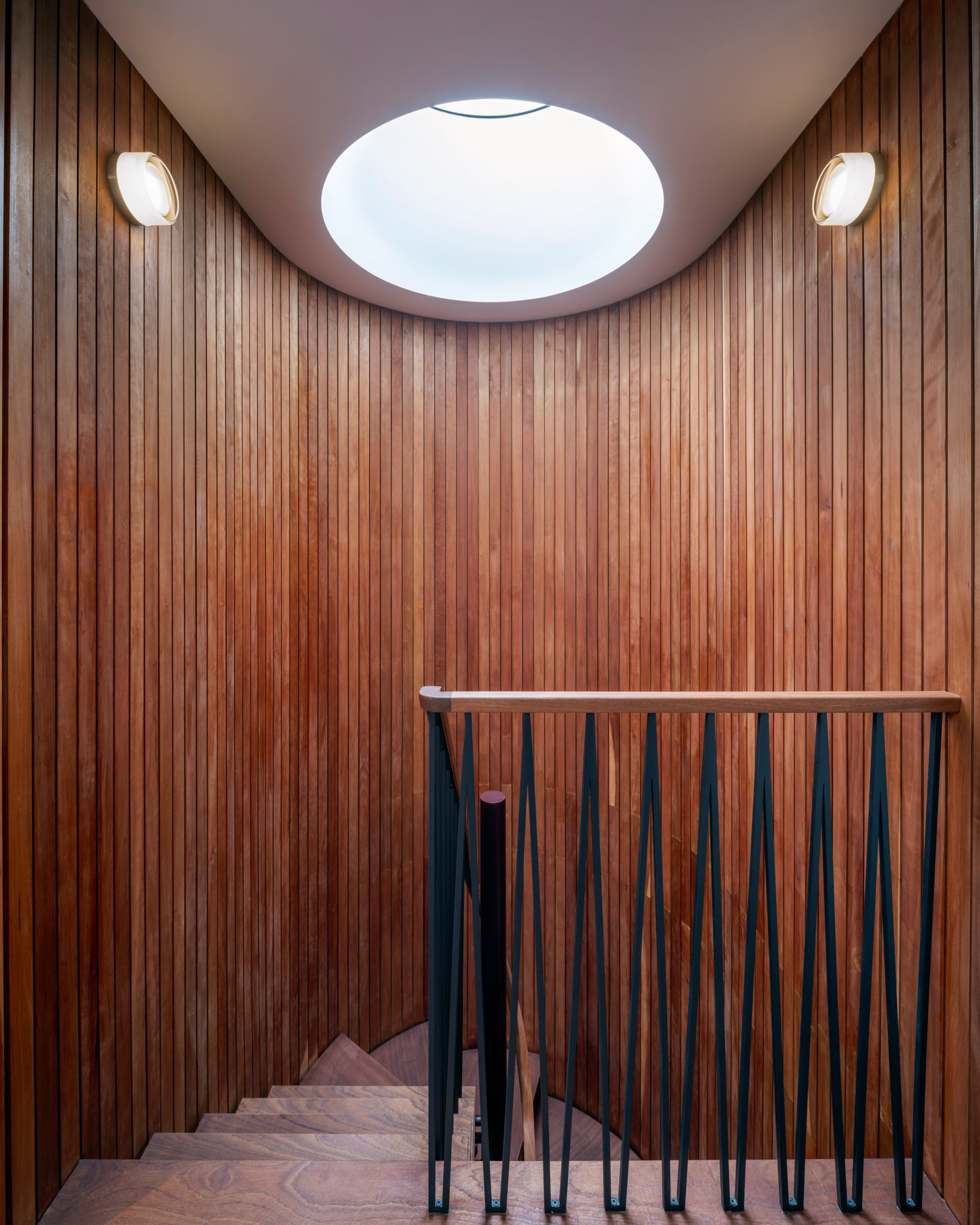 Curved timber staircase beneath a circular skylight