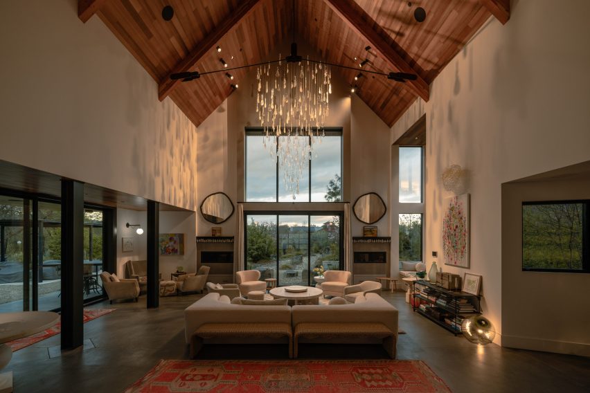 Glass chandelier suspended above a seating area in a double-height living room with a timber ceiling and large windows